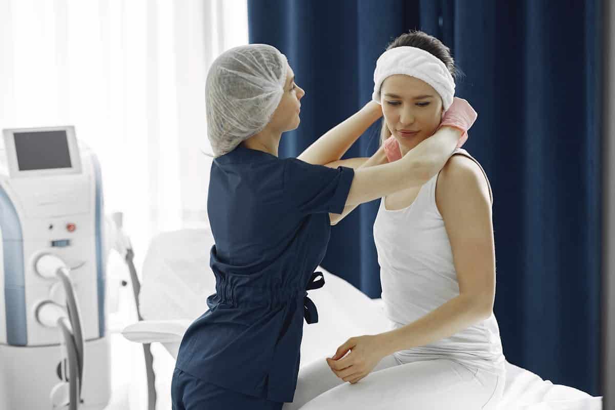 Woman in Blue Scrub Suit Helping Woman Sitting on Bed