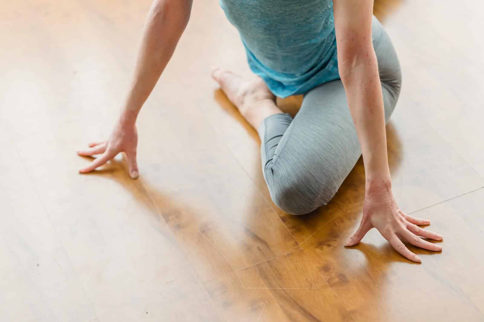 From above of crop anonymous female performing Eka Pada Rajakapotasana on wooden floor at home in daytime