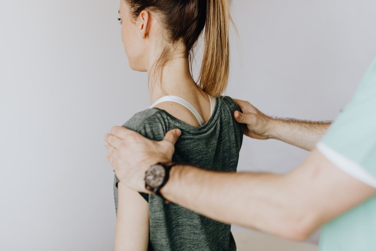 Crop anonymous osteopath straightening shoulders of woman in doctor office